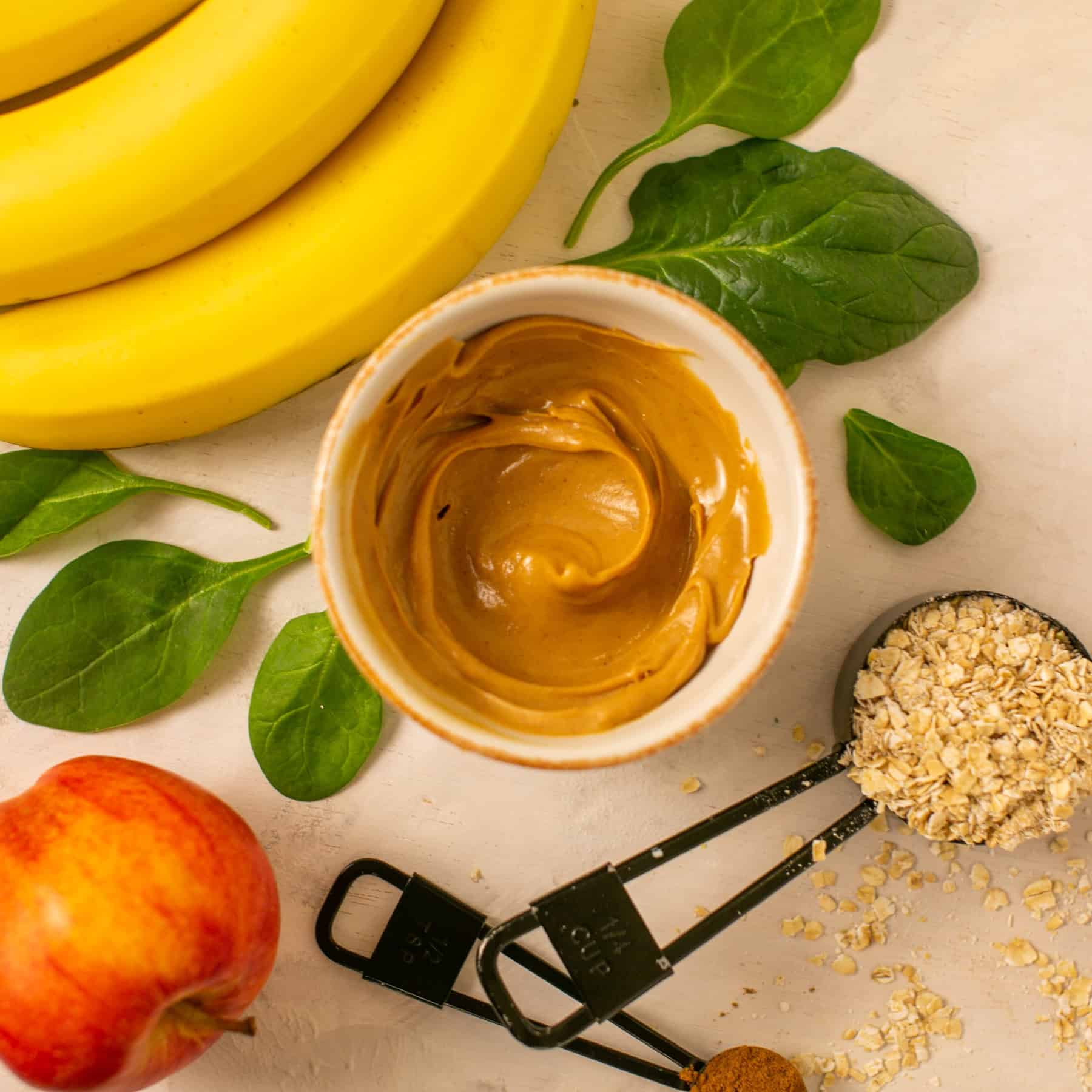 a layout of the ingredients for this healthy smoothie, including a banana, spinach, peanut butter, and oats.