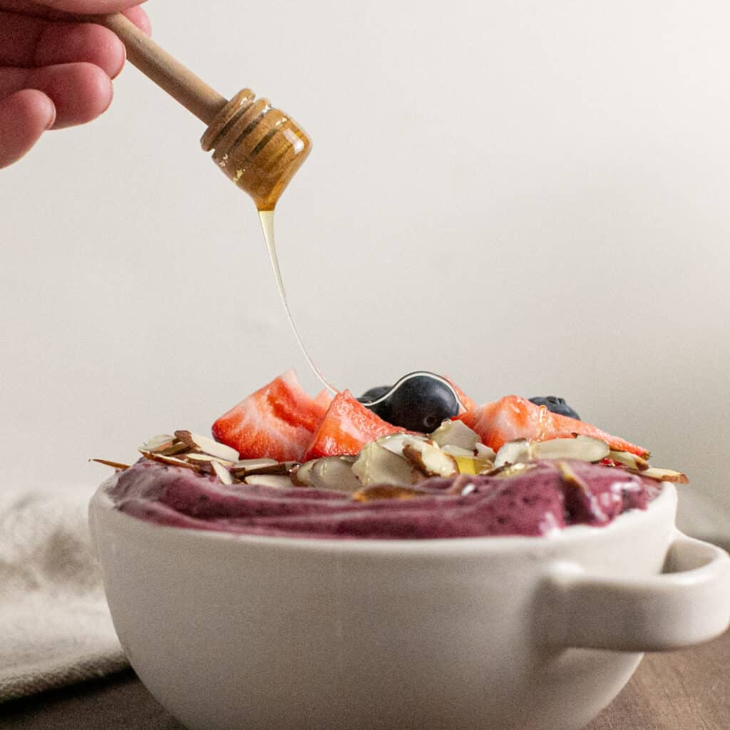 a drizzle shot of honey being drizzled on the berry smoothie bowl.