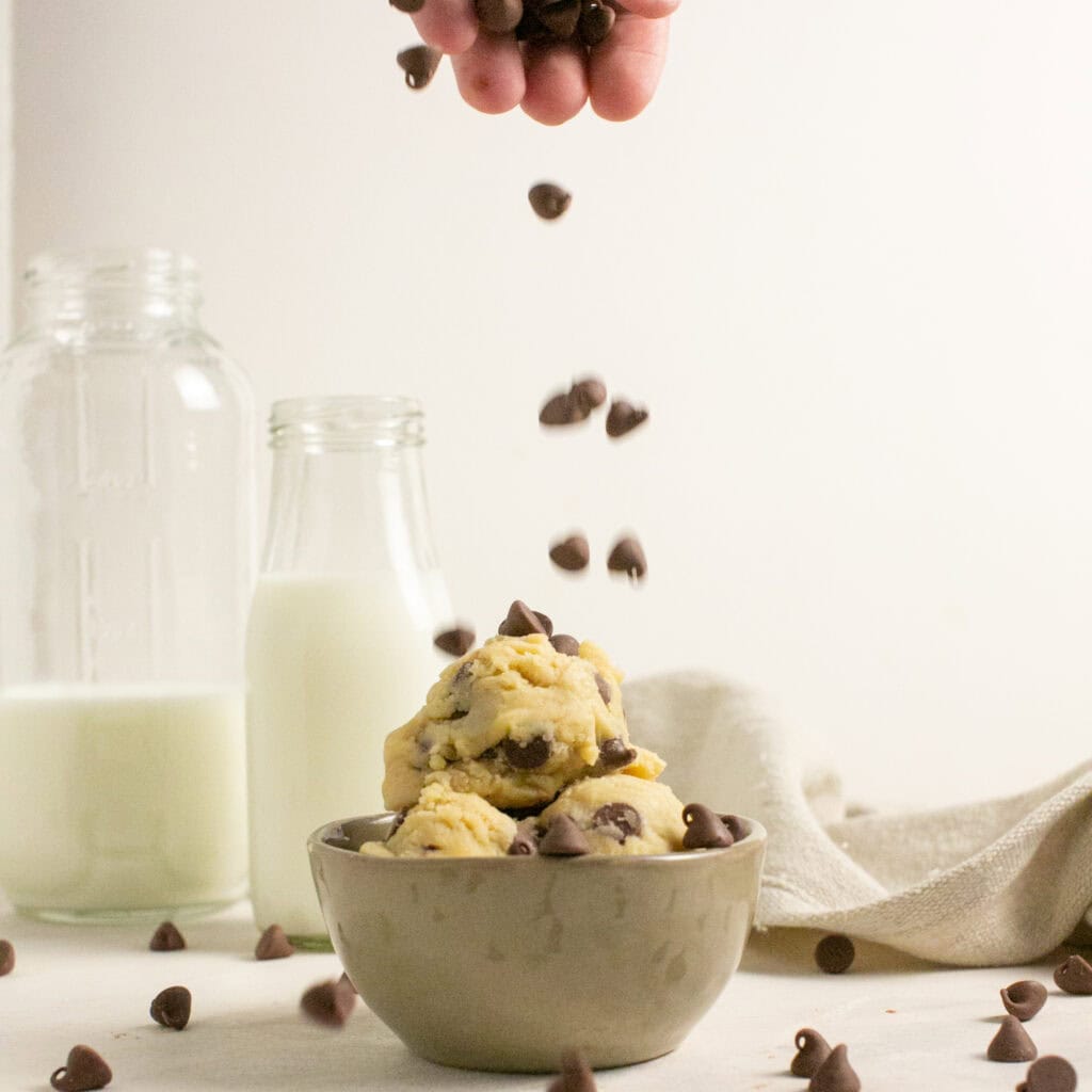 a bunch of chocolate chips being dropped on a bowl of no bake edible cookie dough
