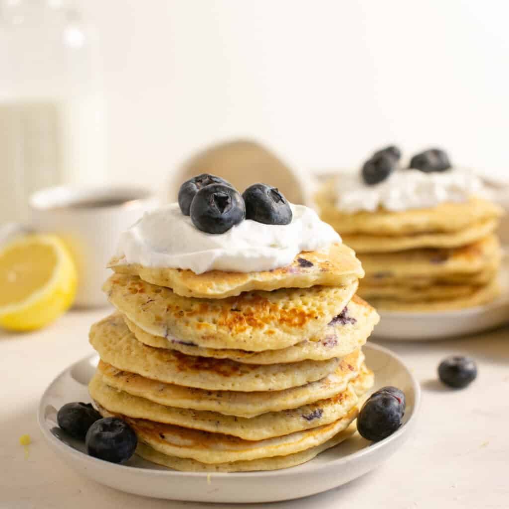 A stack of blueberry pancakes with whipped cream and blueberries on top.
