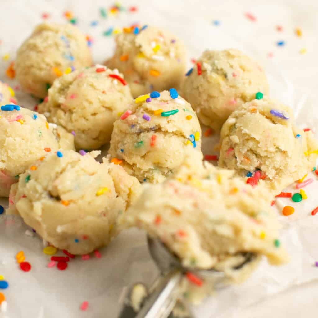 multiple scoops of no bake sugar cookie dough on a cookie sheet.