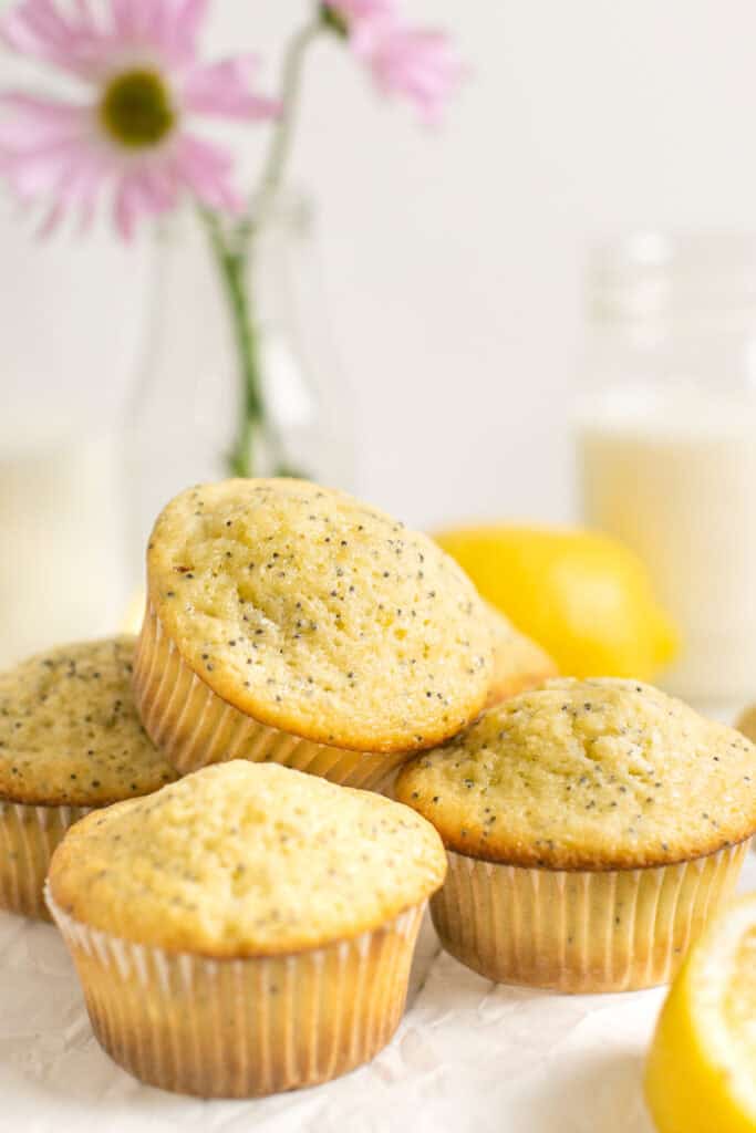 A stack of lemon poppyseed muffins surrounded by lemon slices and a glass of milk