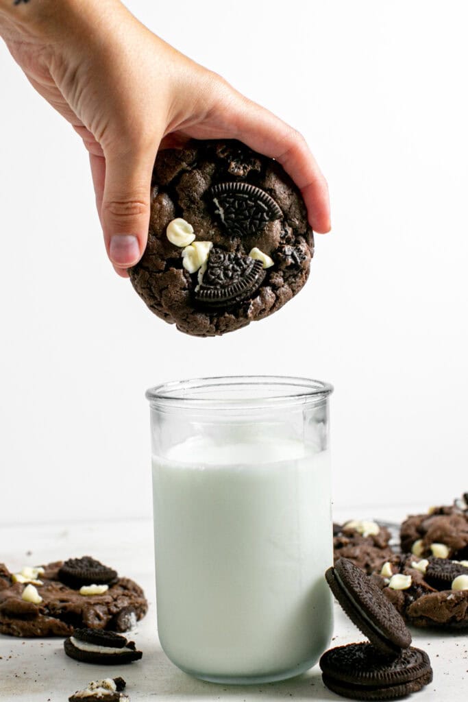 a picture of the cookies n cream cake-mix cookie being held over a glass of milk