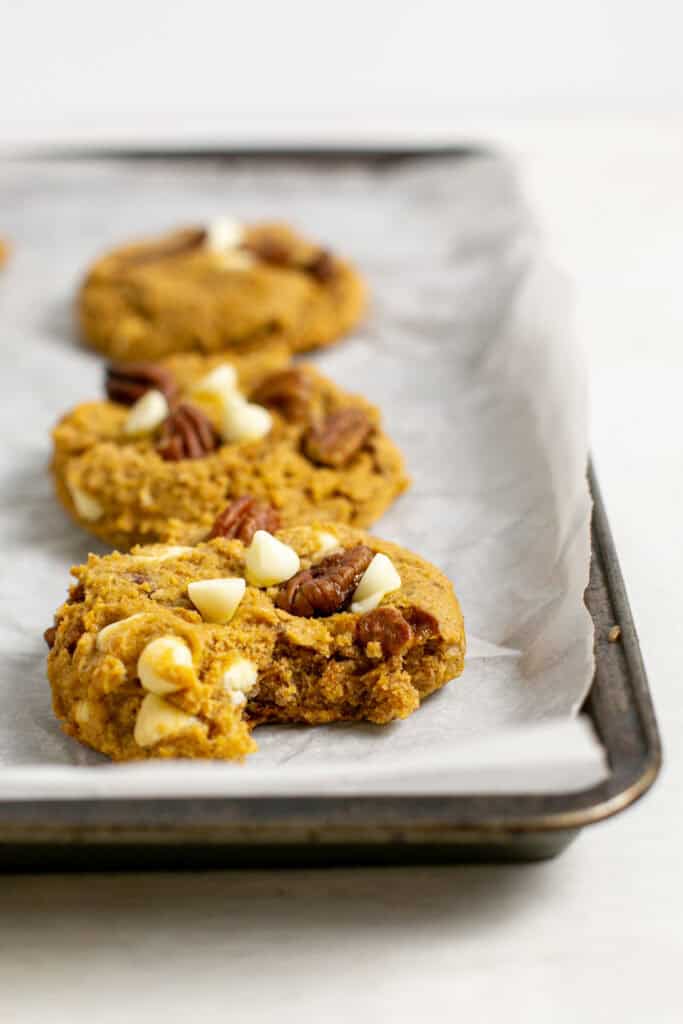 A picture of the cake mix pumpkin cookies sitting on a baking pan with one cookie with a bite taken out