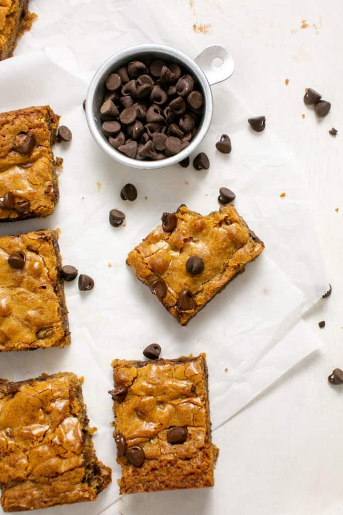 an overhead shot of the chocolate chip blondies with a bite taken out sitting by a measuring cup with chocolate chips.
