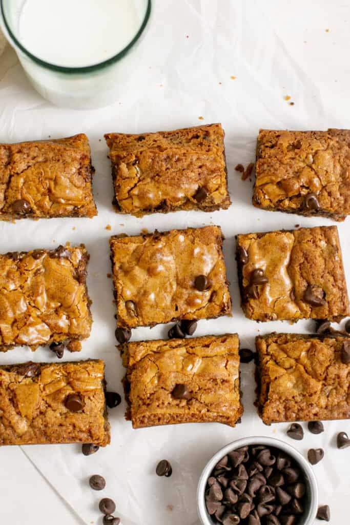 an overhead shot of the chocolate chip blondies with a glass of milk in one corner and a measuring cup of chocolate chips in the other corner