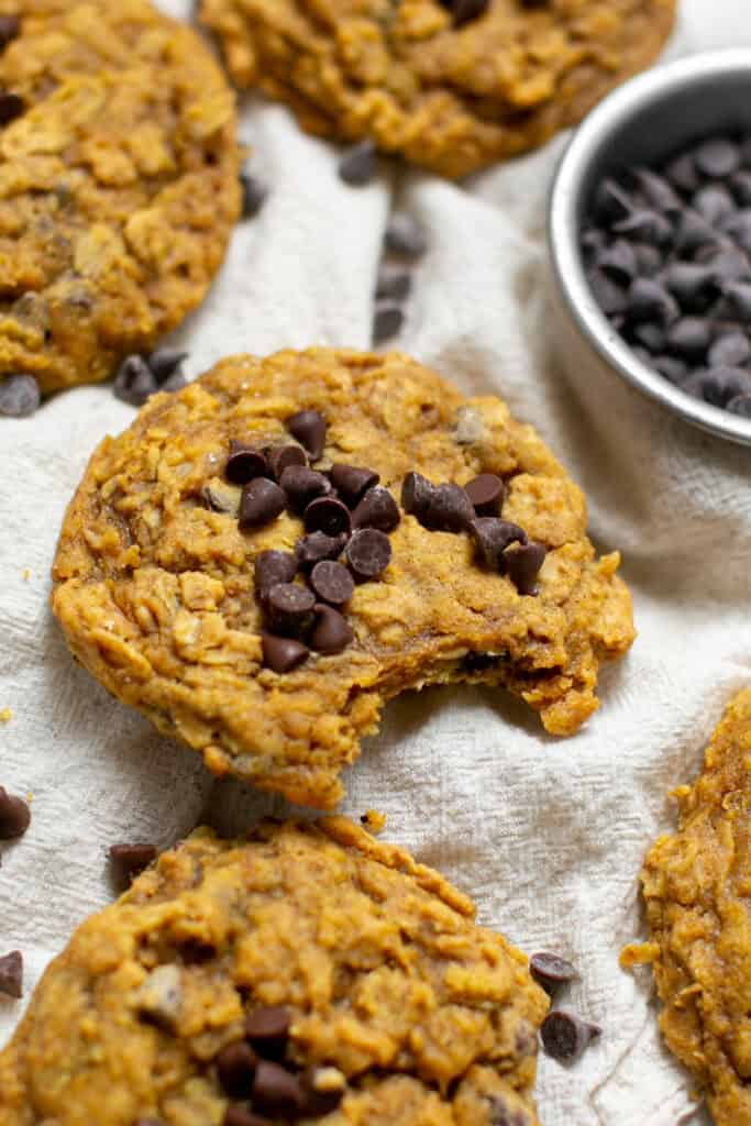 A pumpkin oatmeal cookie sitting on a linen towel with chocolate chips around.