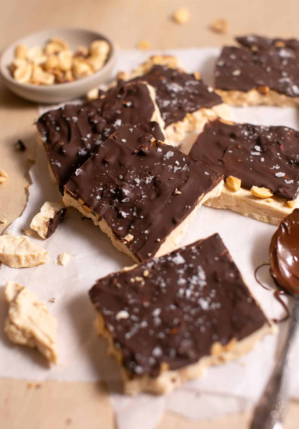Pieces of Peanut Butter Yogurt Bark by a bowl of peanuts. 