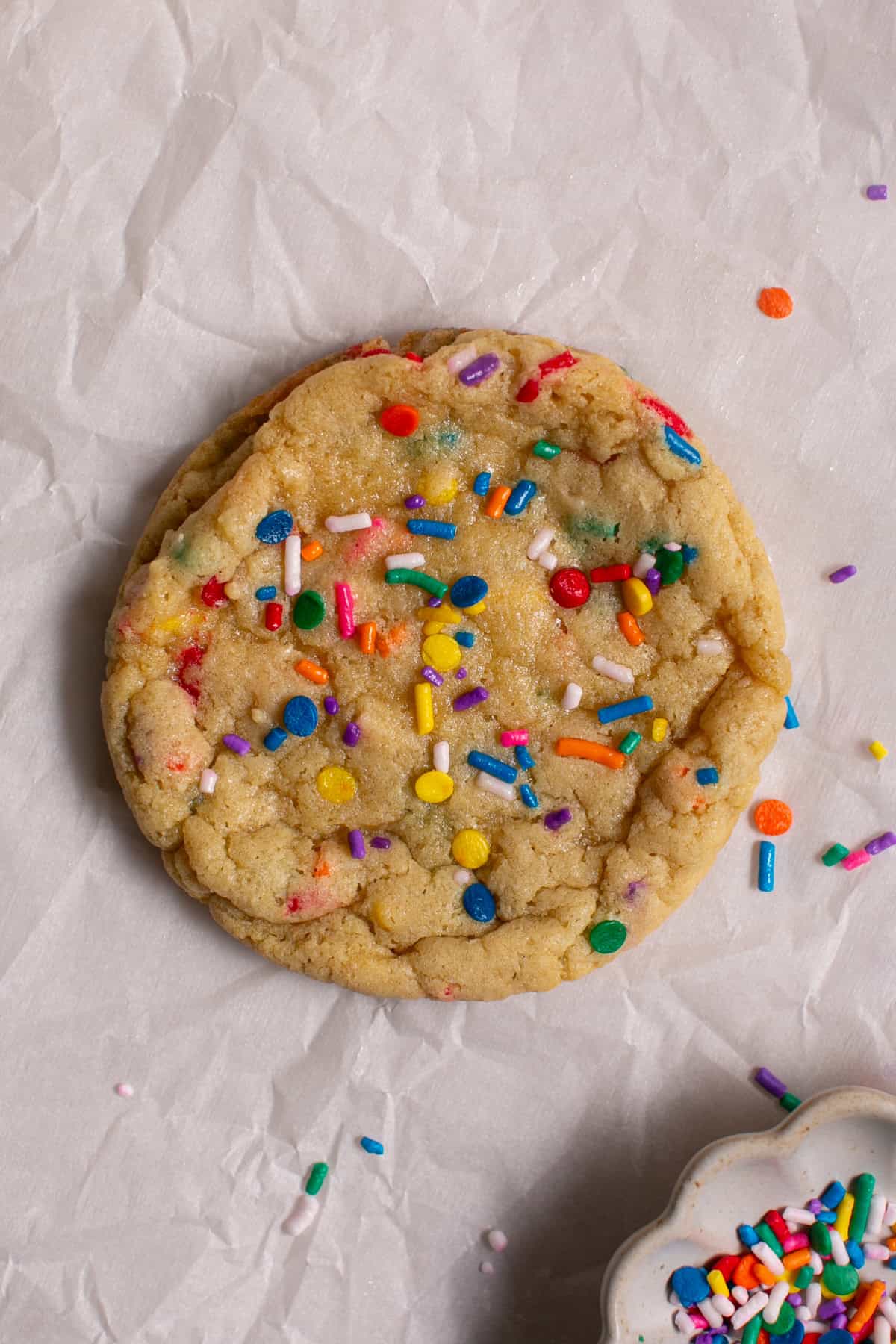 Single Serve Sugar Cookie sitting by some sprinkles on parchment paper. 