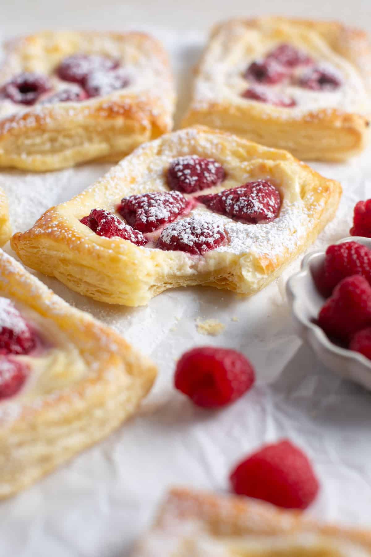 Raspberry Cream Cheese Danish with a bite missing and some crumbs beside it. 