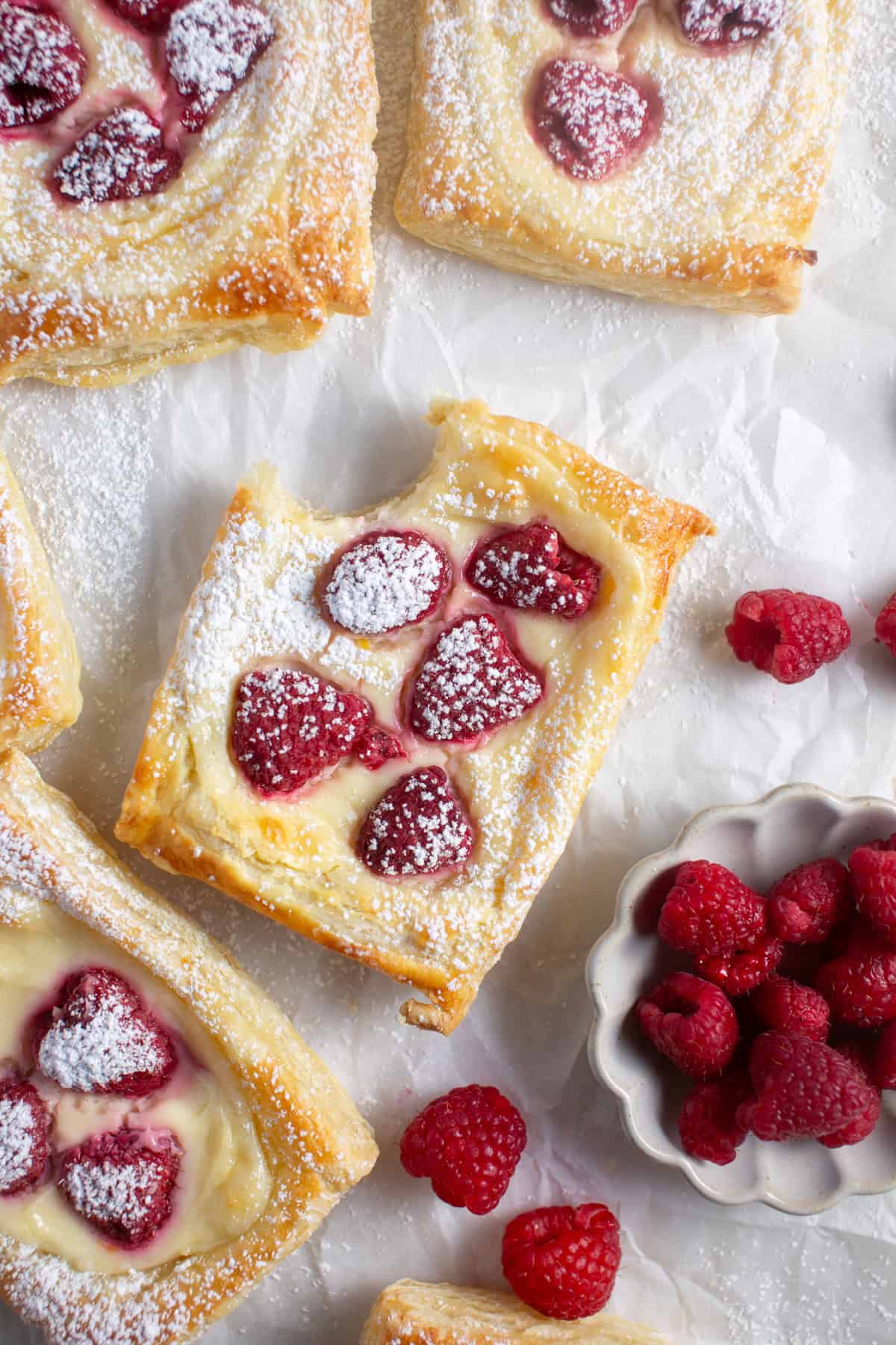 Raspberry Cream Cheese Danish with a bite missing by a bowl of raspberries.