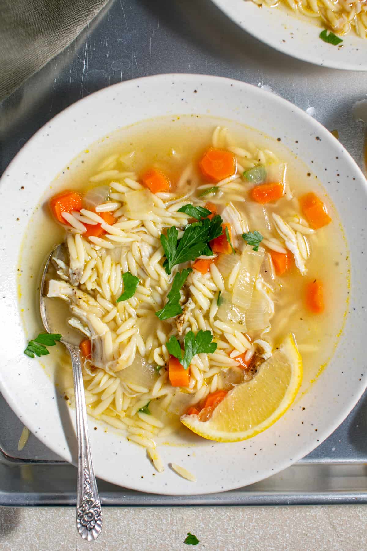 Lemon orzo soup with a soup sitting beside it. 