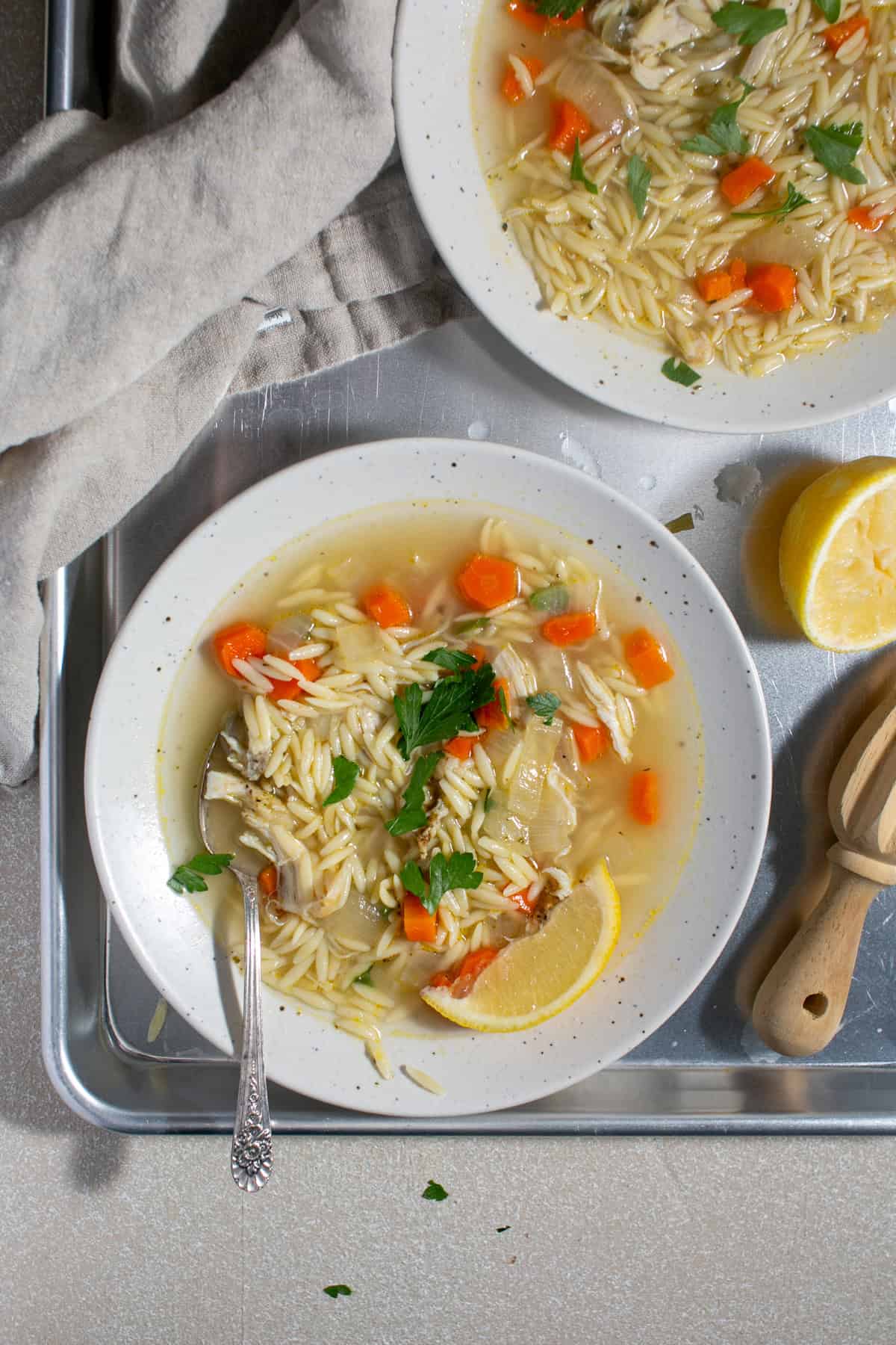 Lemon orzo soup sitting on a tray with two bowls of soup.