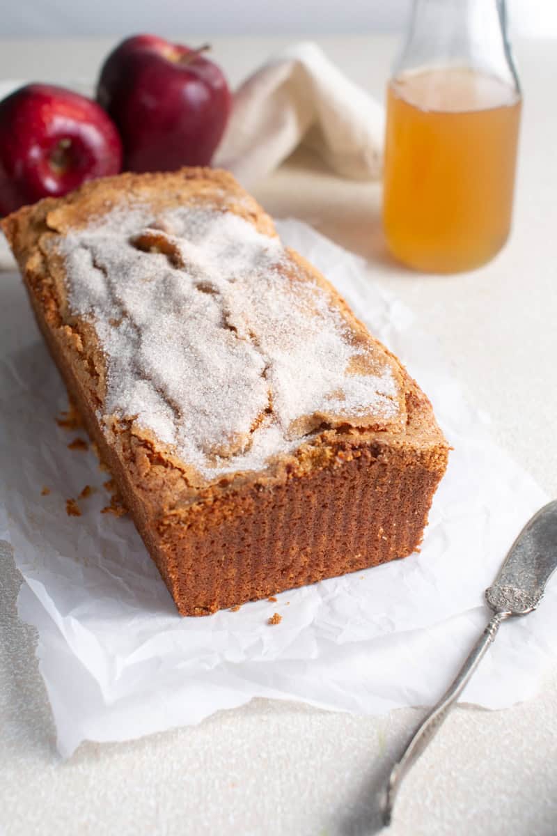 Apple Cider loaf on parchment paper with apple cider beside it.