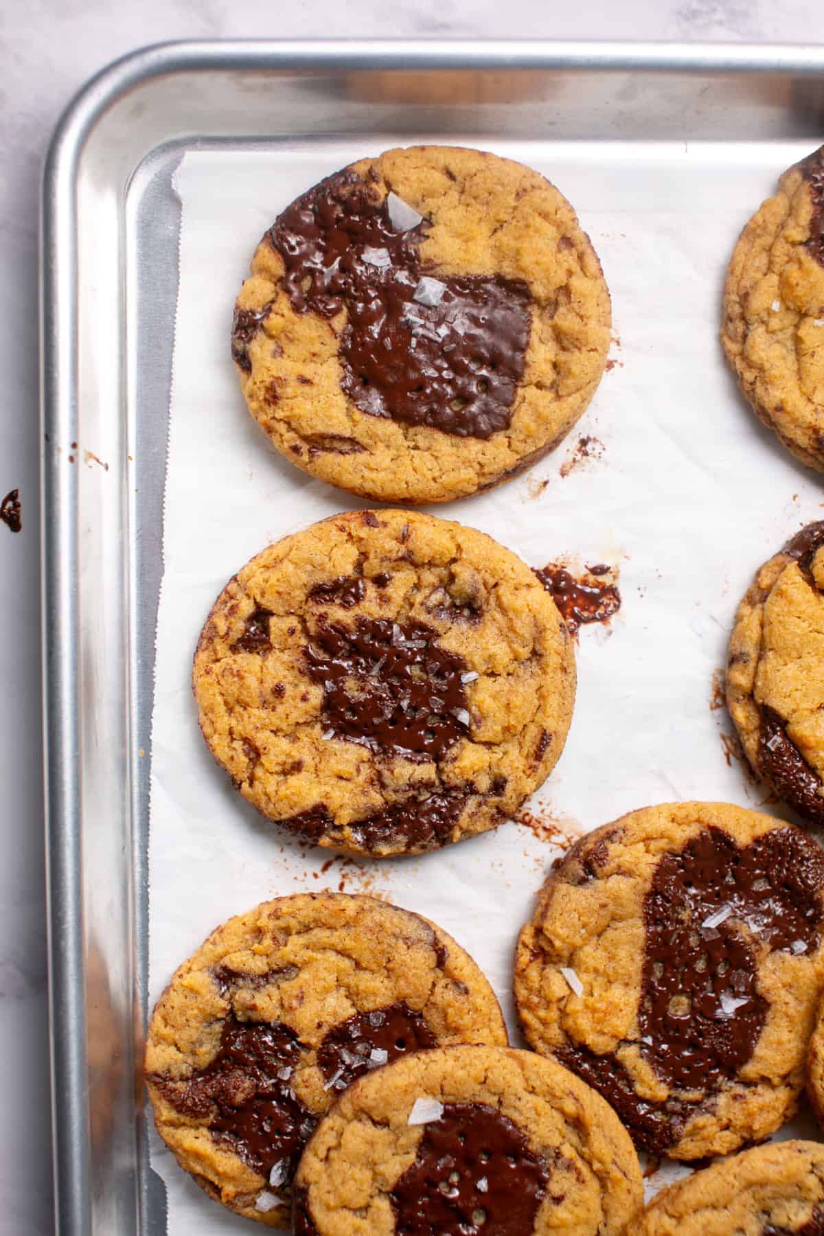 Thick and Chewy Pumpkin Dark Chocolate Chunk Cookies on a sheet pan with smeared chocolate.