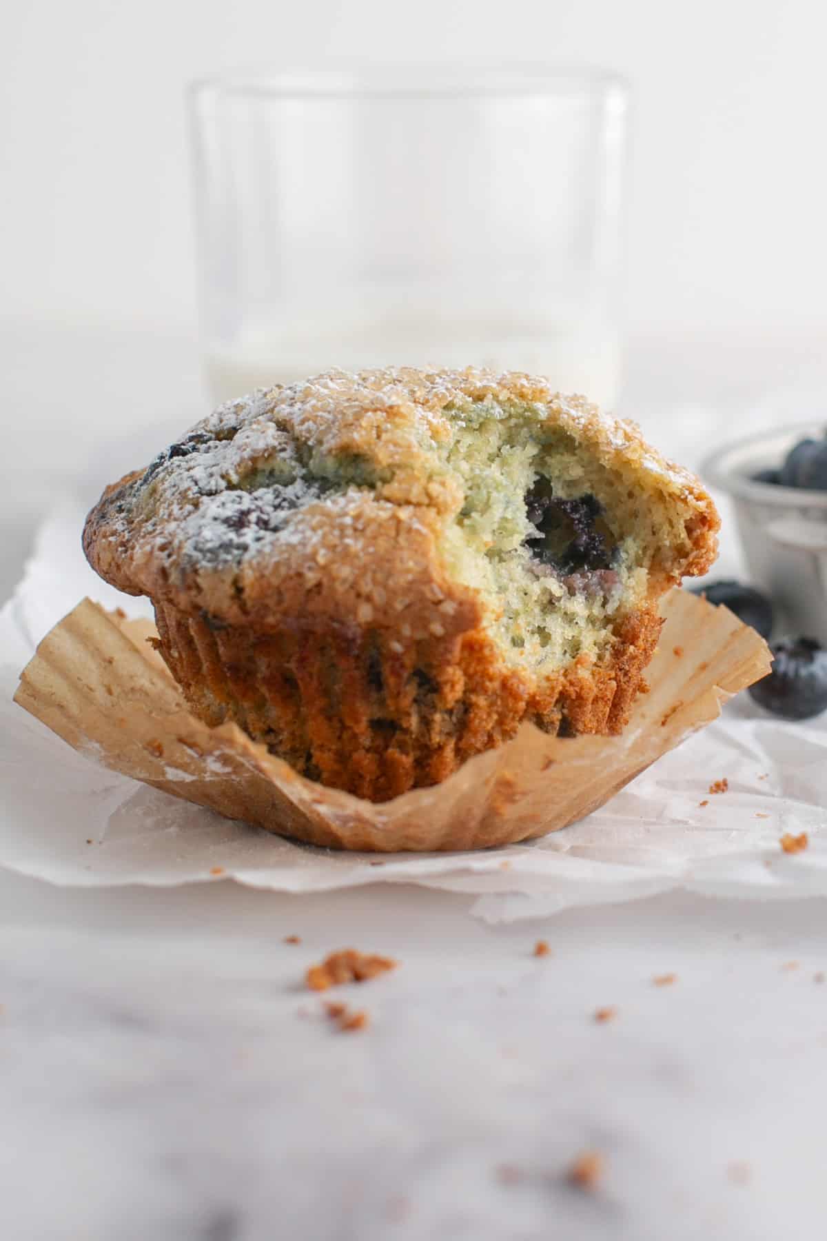 Single Serve Blueberry Muffin with a bite missing by a glass of milk.